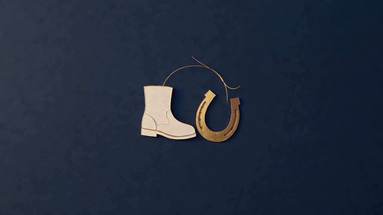 Paper-cut still life of a walking boot, a small horseshoe and a winding gold thread on navy