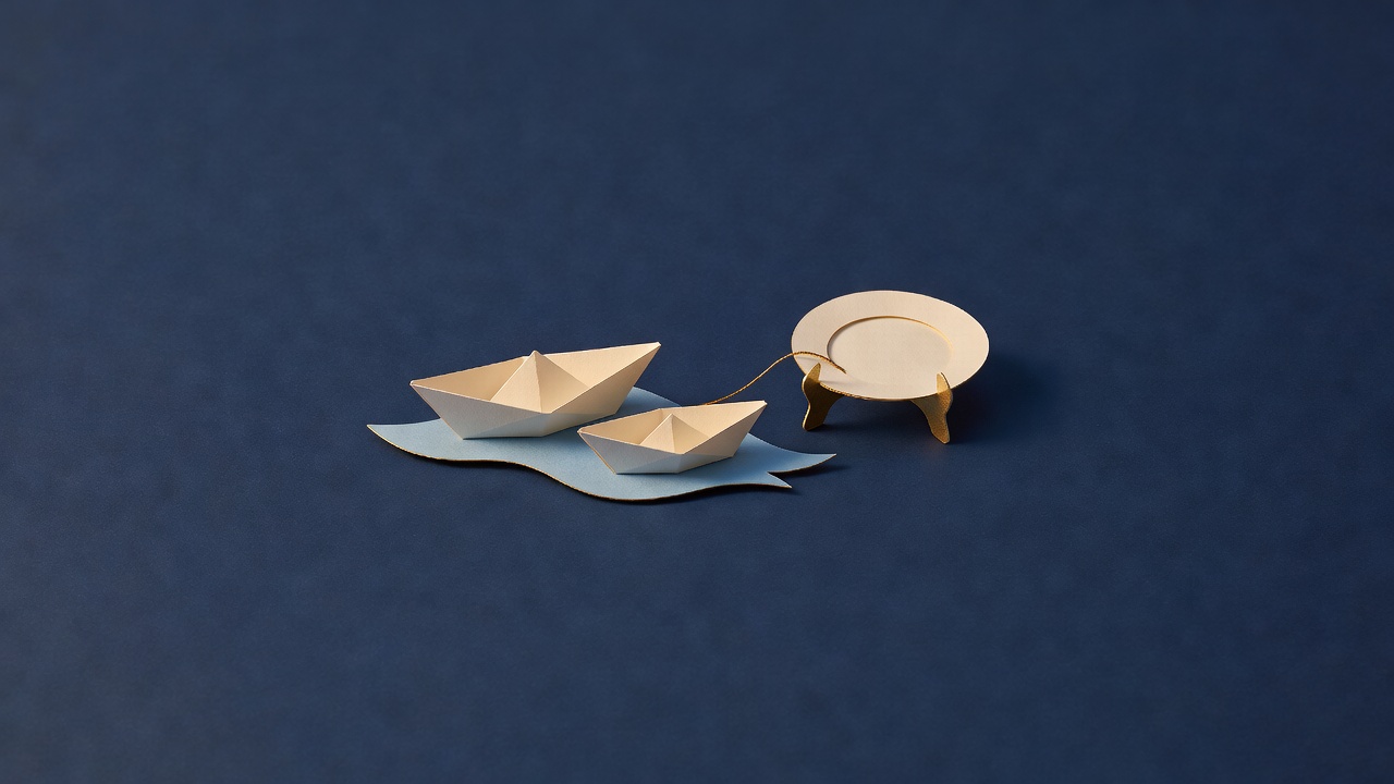 Paper-cut still life of two plain paper boats on a blue ribbon of water beside a plate on a gold stand, on navy