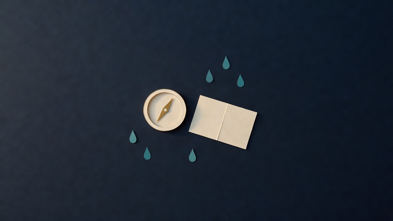 Paper-cut still life of a plain paper compass, a folded blank ticket and teal raindrops on navy