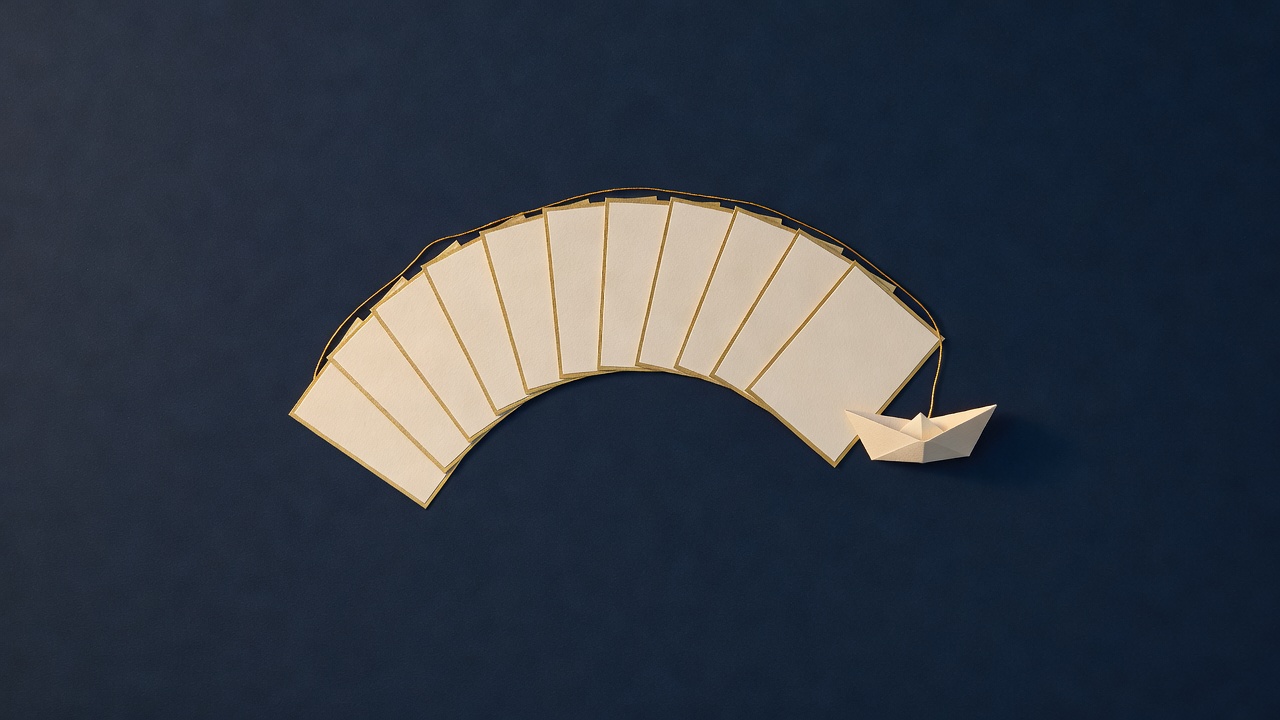 Paper-cut still life of a fan of blank cards in an arc beside a small paper boat and a gold thread on navy