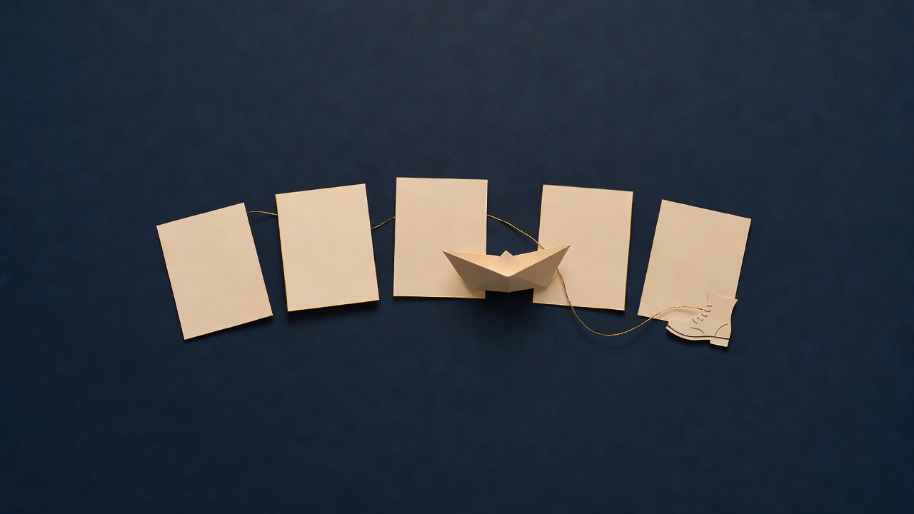 Paper-cut still life of five blank cards in a row with a small paper boat and a walking boot on navy