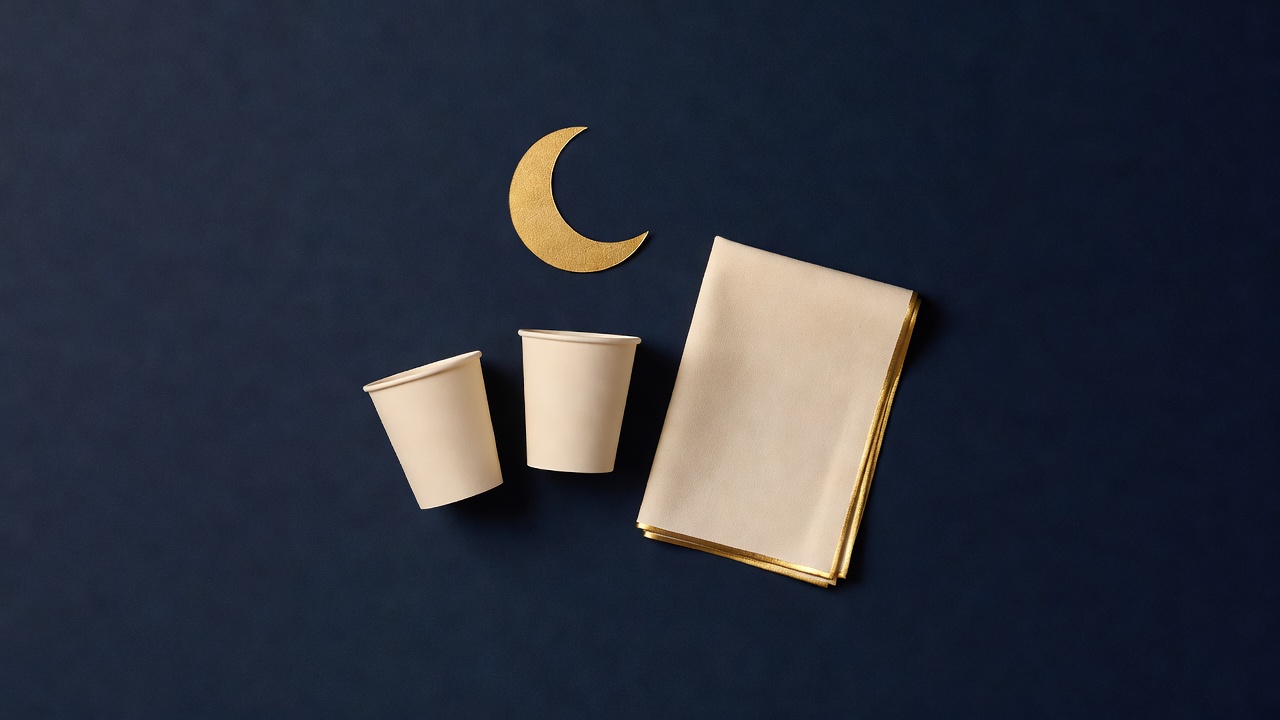 Paper-cut still life of two cups, a folded blanket and a crescent moon on navy