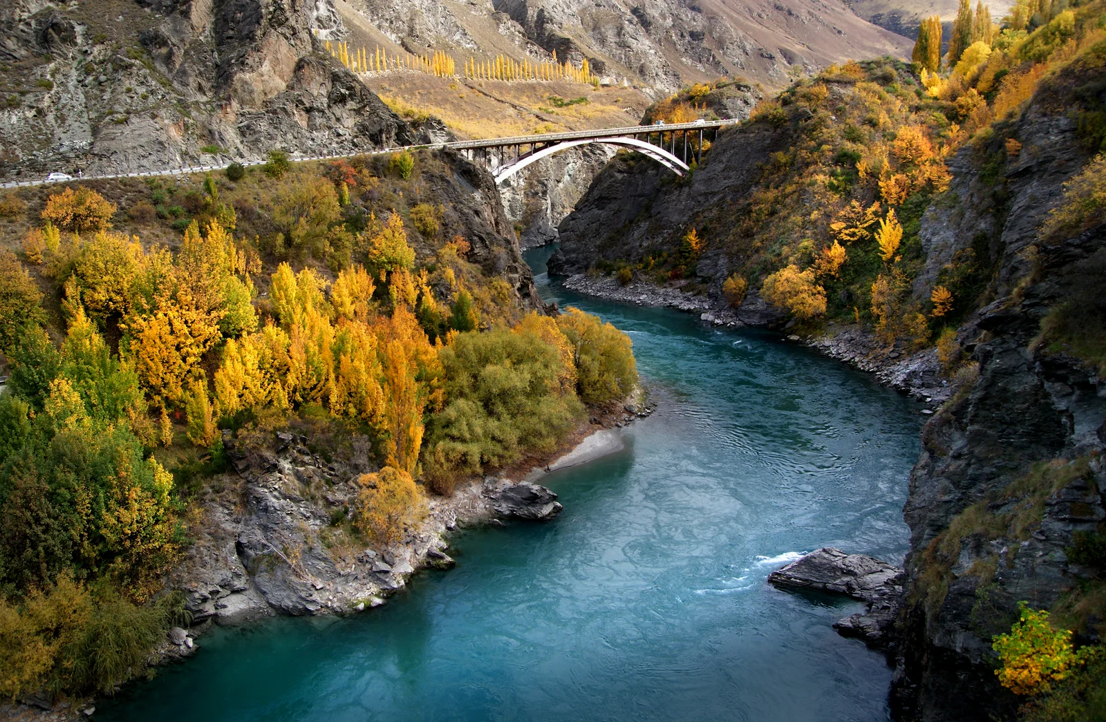 Archive view of the Kawarau River between rocky slopes, with autumn trees and a road bridge.