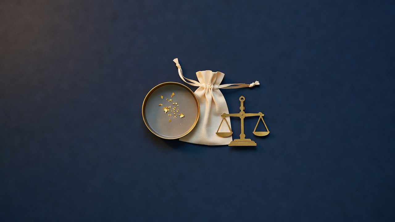 Paper-cut still life of a gold pan with gold flakes, a drawstring pouch and a small balance scale on navy