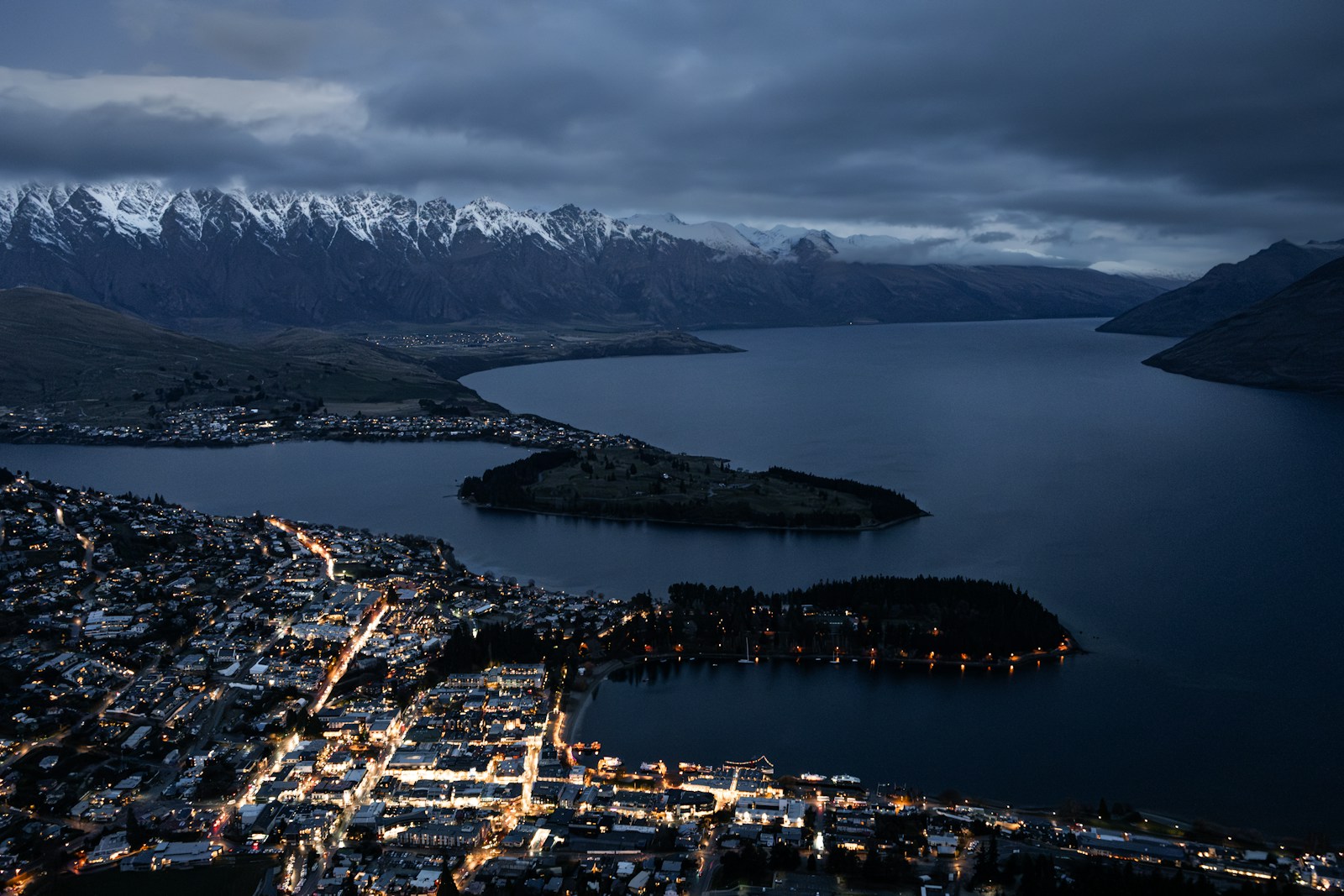 Queenstown town lights twinkling at night with the mountains behind